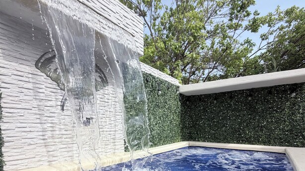 Un bain à remous agrémenté d’une cascade, entouré d’un mur de pierres et d’une haie verdoyante.