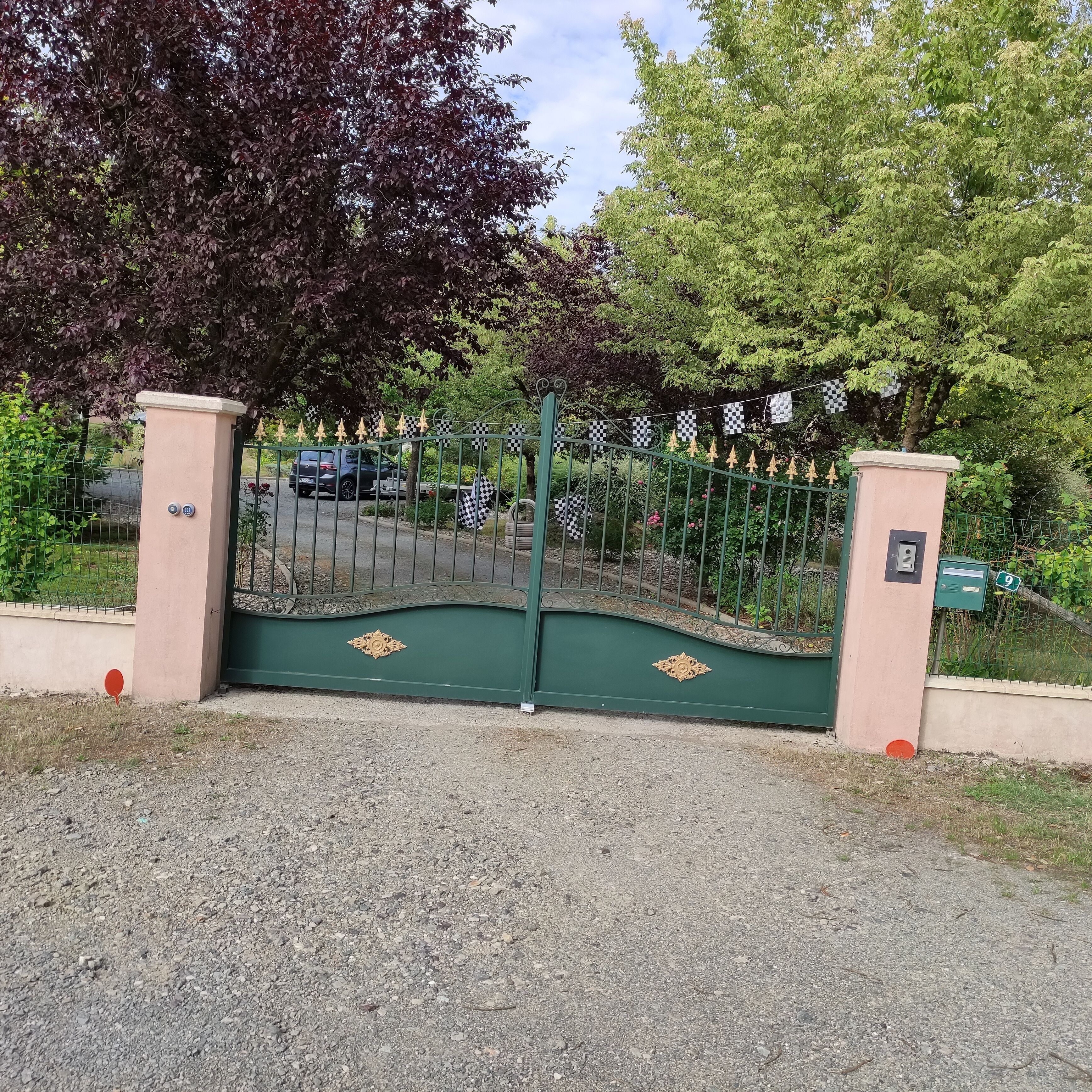 A gated entrance with decorative elements, a gravel driveway, and a vehicle parked inside.