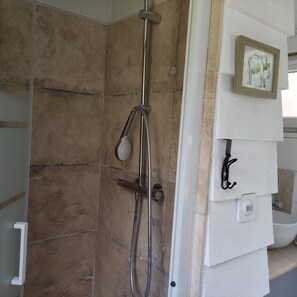 Una ducha con cabezal de ducha de mano y grifo empotrado, un cuadro en la pared, y una puerta blanca con manija.