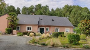 Een huis met één verdieping, een grijs dak, een groene deur en een oprit met grind.