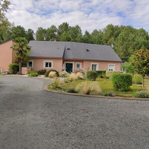 A single-story house with a grey roof, a green door, and a gravel driveway. - "L'oasis des pins" House 12 pers+ swimming pool 20mm from Le MANS (Château-l'Hermitage)