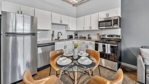 A modern kitchen with white cabinets, stainless steel appliances, and a dining area with a glass table and brown chairs. - Cold Storage by Stylish Stays (Kansas City)