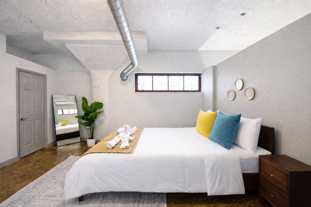 A bedroom with a bed, bedside table, potted plant, and a window.