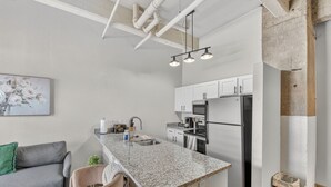 A modern kitchen with a granite countertop, stainless steel appliances, and a dining area with a gray sofa and chairs. - Cold Storage by Stylish Stays (Kansas City)