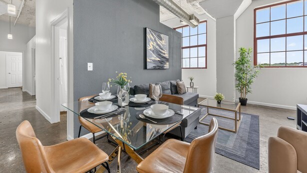 A modern dining area with a glass table, leather chairs, a gray accent wall, and a large window. - Cold Storage by Stylish Stays (Kansas City)