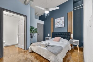 A bedroom with a bed, bedside tables, a ceiling fan, a door, and a wall-mounted artwork. - Cold Storage by Stylish Stays (Kansas City)