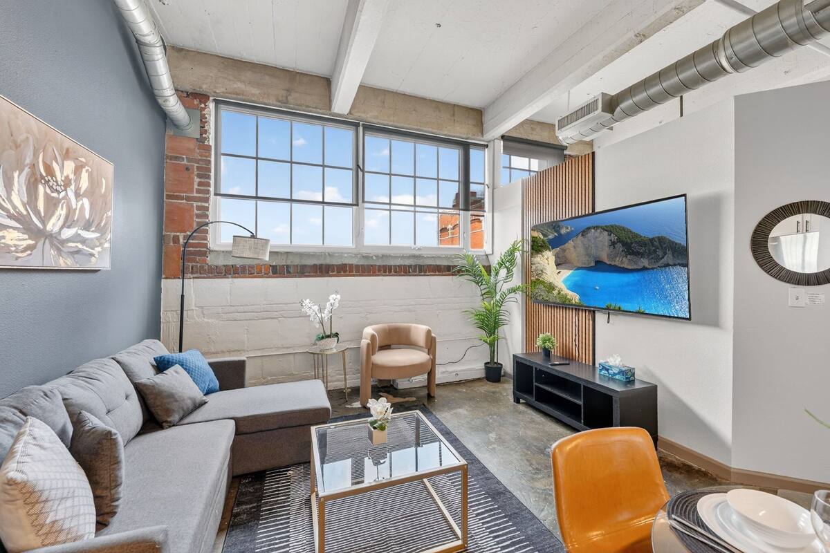A modern living room with a sofa, armchair, coffee table, TV, and a large window with a view.