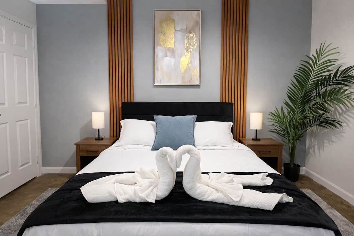 A hotel room with a bed, two bedside tables, a wall-mounted artwork, a potted plant, and a door.