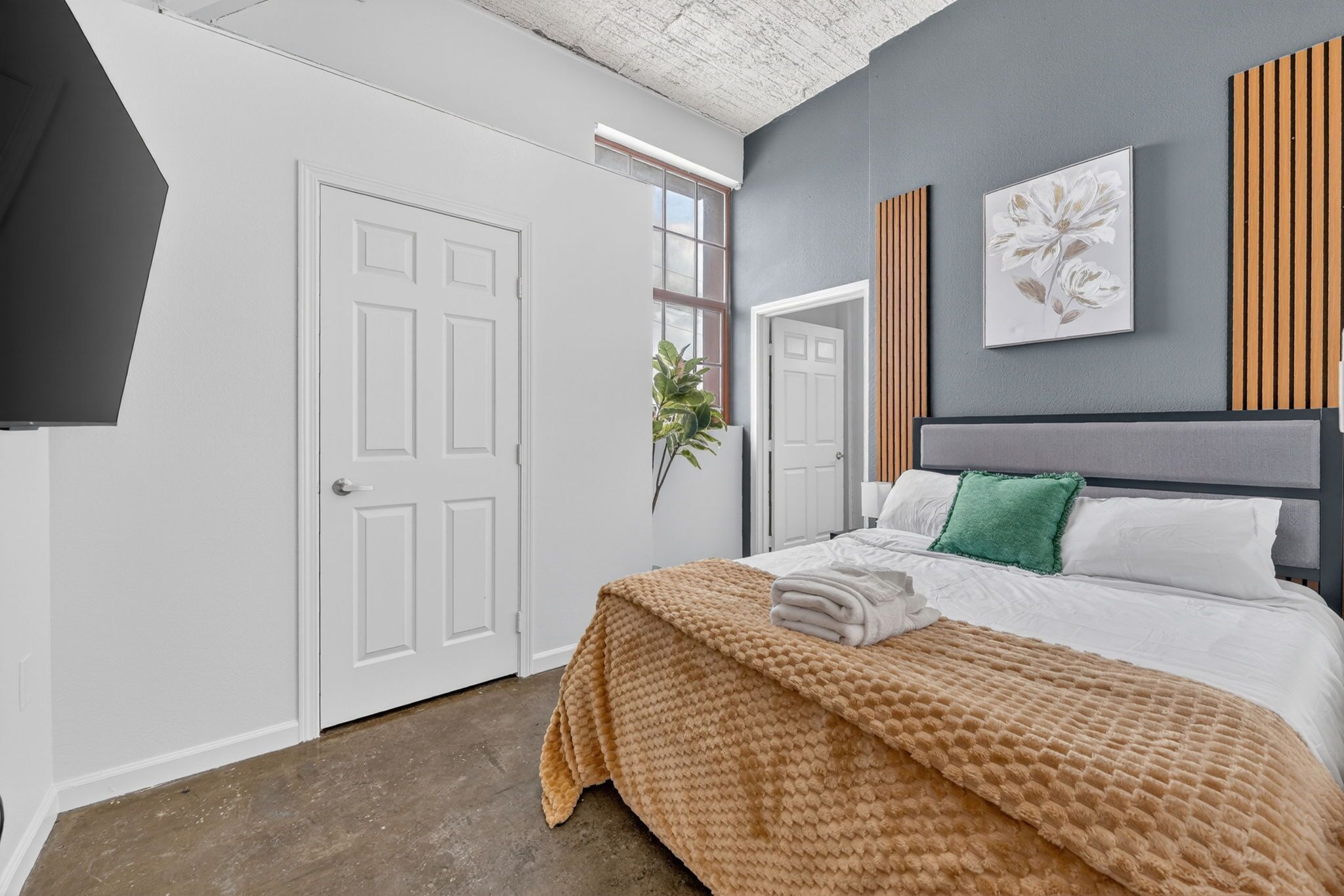 A bedroom with a bed, a window, a door, and a wall-mounted artwork.