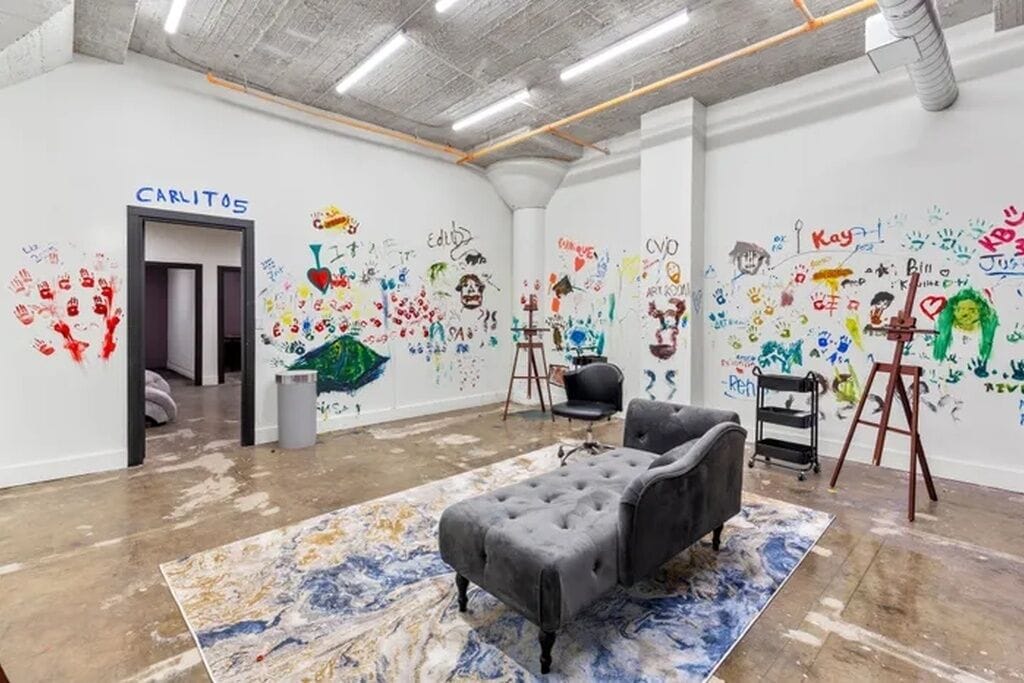 Una galería de arte con un sofá negro, un tapete con estampado de mármol y paredes cubiertas de huellas de manos y dibujos coloridos.