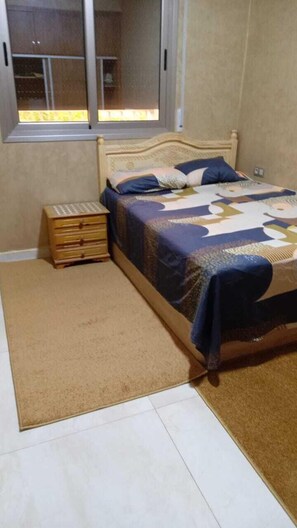 A bedroom with a bed, a wooden nightstand, a window, and a door.