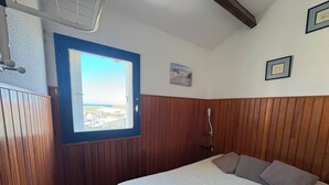 Un dormitori amb paret de fusta panelada, finestra amb vistes, llit amb almoadines i una petita taula de nit.
