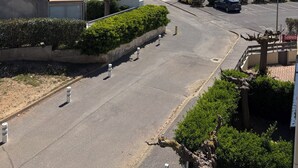 Un carrer residencial amb cotxes aparcats, cel serena i vista del mar a la distància.