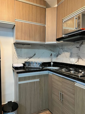 A modern kitchen with wooden cabinets, a black countertop, a stove, and a microwave. - Oceana Suites Cartagena de Indias (Cartagena)