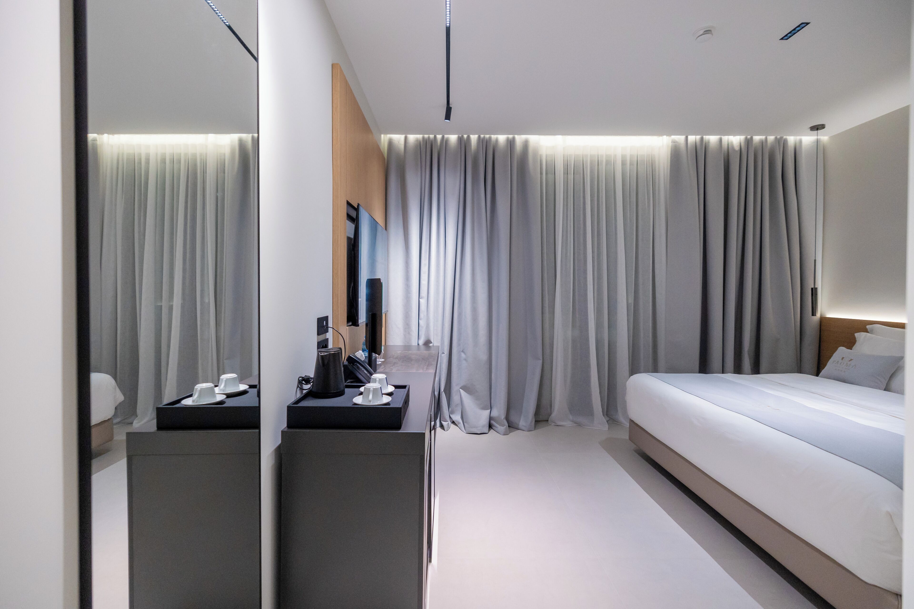 Een moderne hotelkamer met een groot bed, een bureau met een computer, een spiegel en uitzicht op de kamer door een raam met gordijnen.