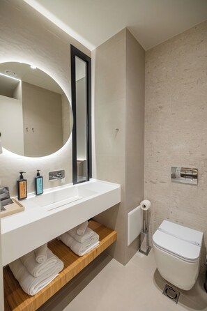 Un baño moderno con lavamanos, espejo y retrete blancos.