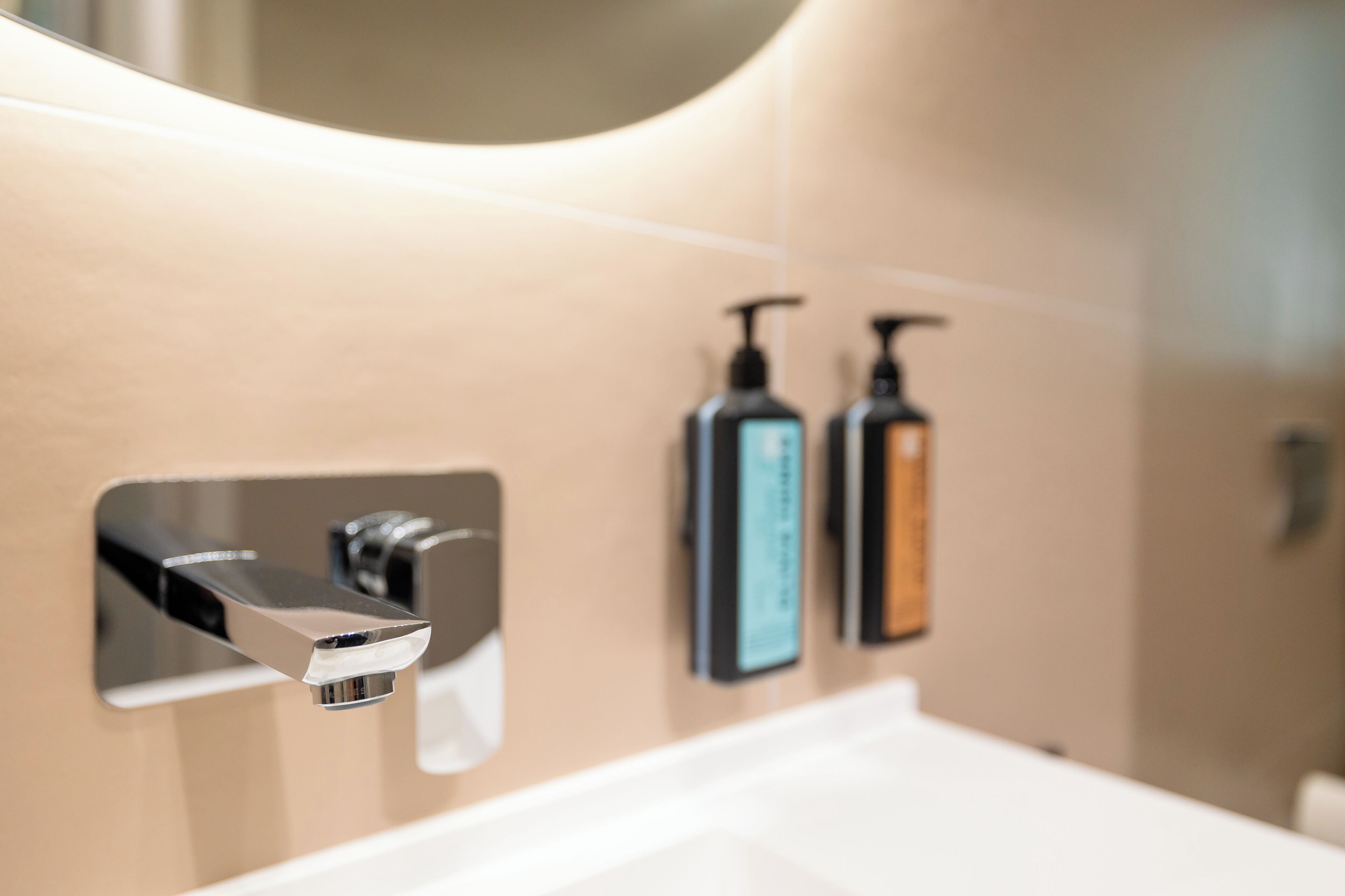 Une salle de bain équipée d’un robinet moderne, d’un miroir et de deux distributeurs de savon.