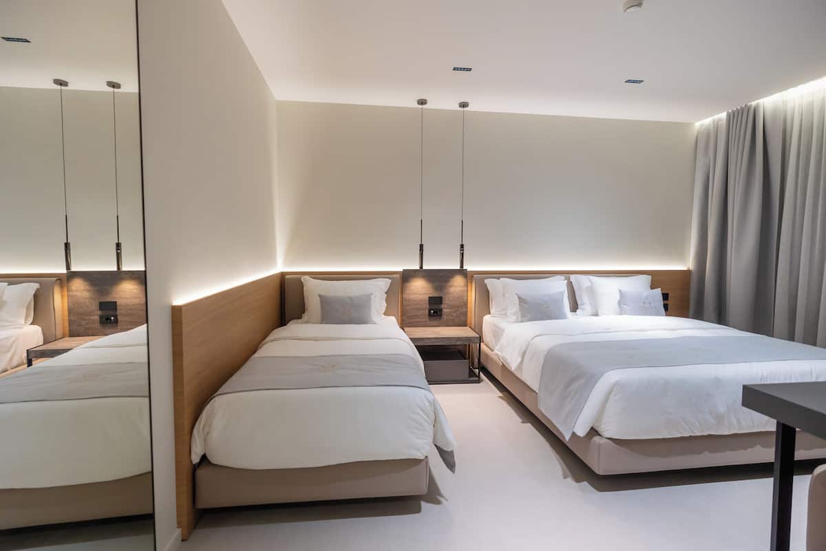 A modern hotel room with two beds, a wooden headboard, a bedside table, and a mirror.