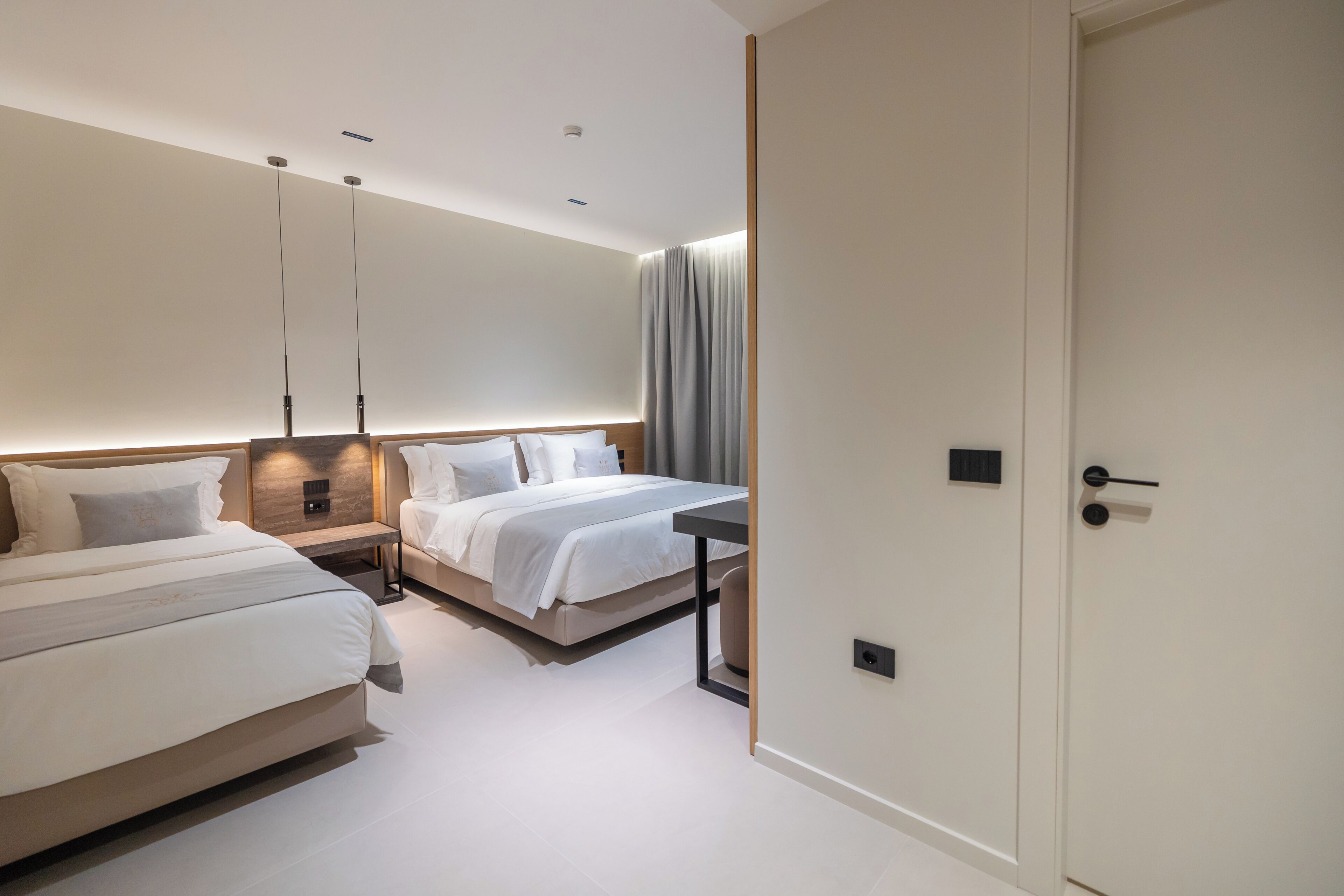 Ein modernes Hotelzimmer mit zwei Betten, einem Nachttisch, einem Schreibtisch und einer Tür.