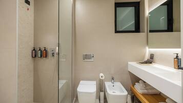 Un baño moderno con mampara de vidrio, inodoro, bidé y tocador con espejo y toallero.