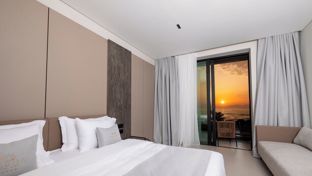 A hotel room with a bed, a sofa, and a balcony with a view of the sunset. - Padma Hotel (Vlorë)