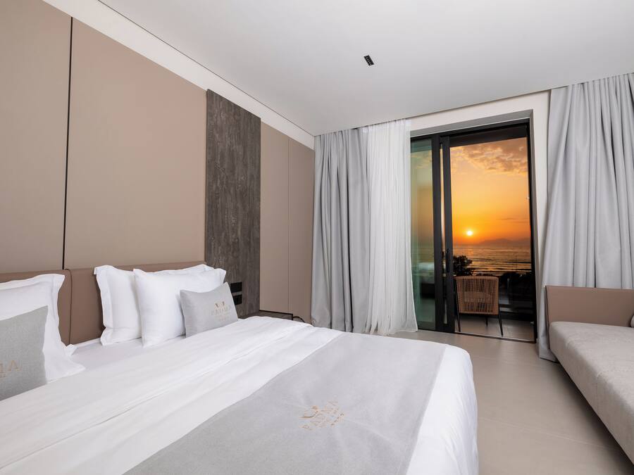 Habitación de hotel con cama, sofá y balcón con vista al atardecer.