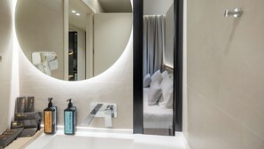 A modern bathroom with a round mirror, a towel rack, and toiletries on the counter. - Padma Hotel (Vlorë)