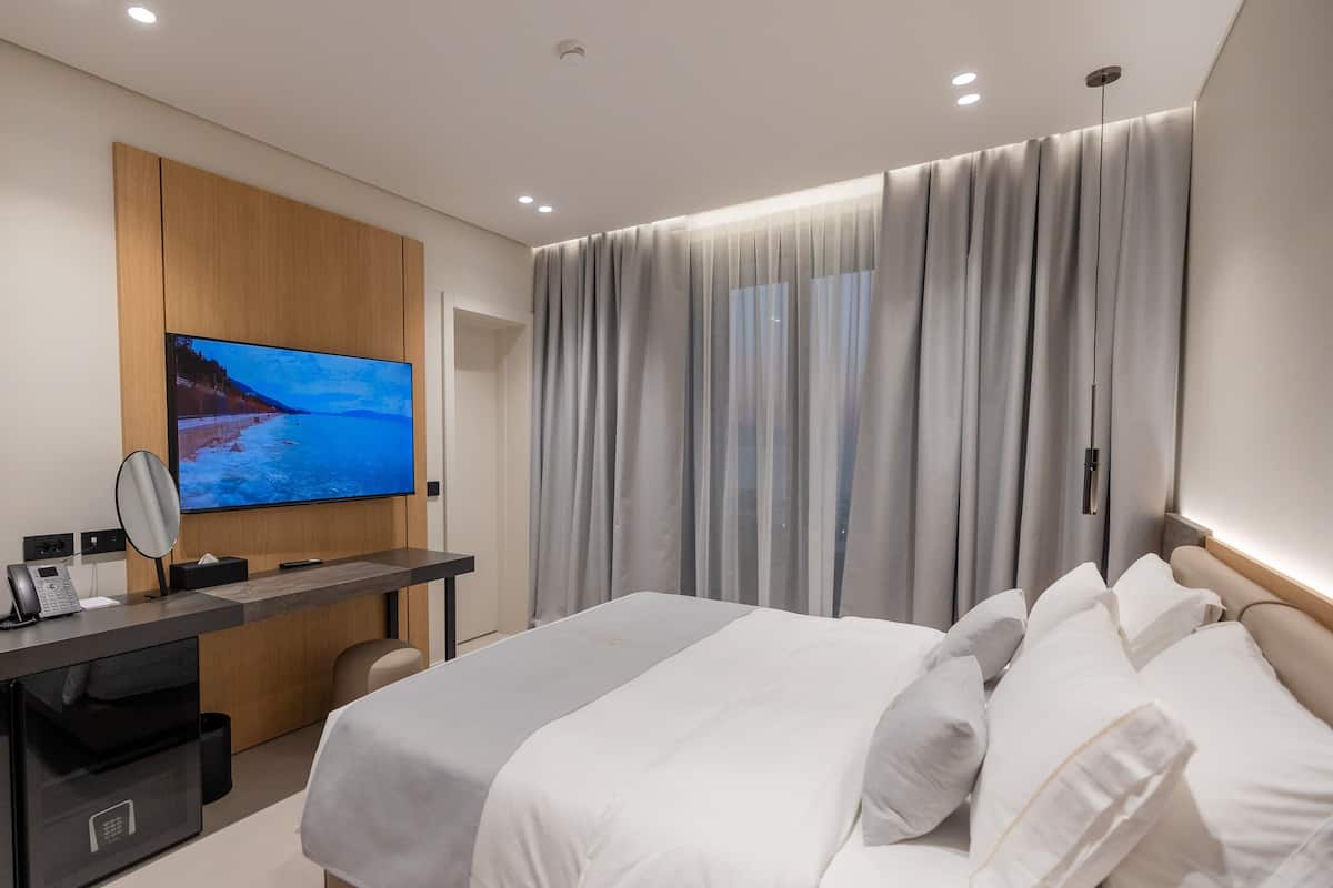 A modern hotel room with a bed, a desk with a computer, a TV, and a bathroom.