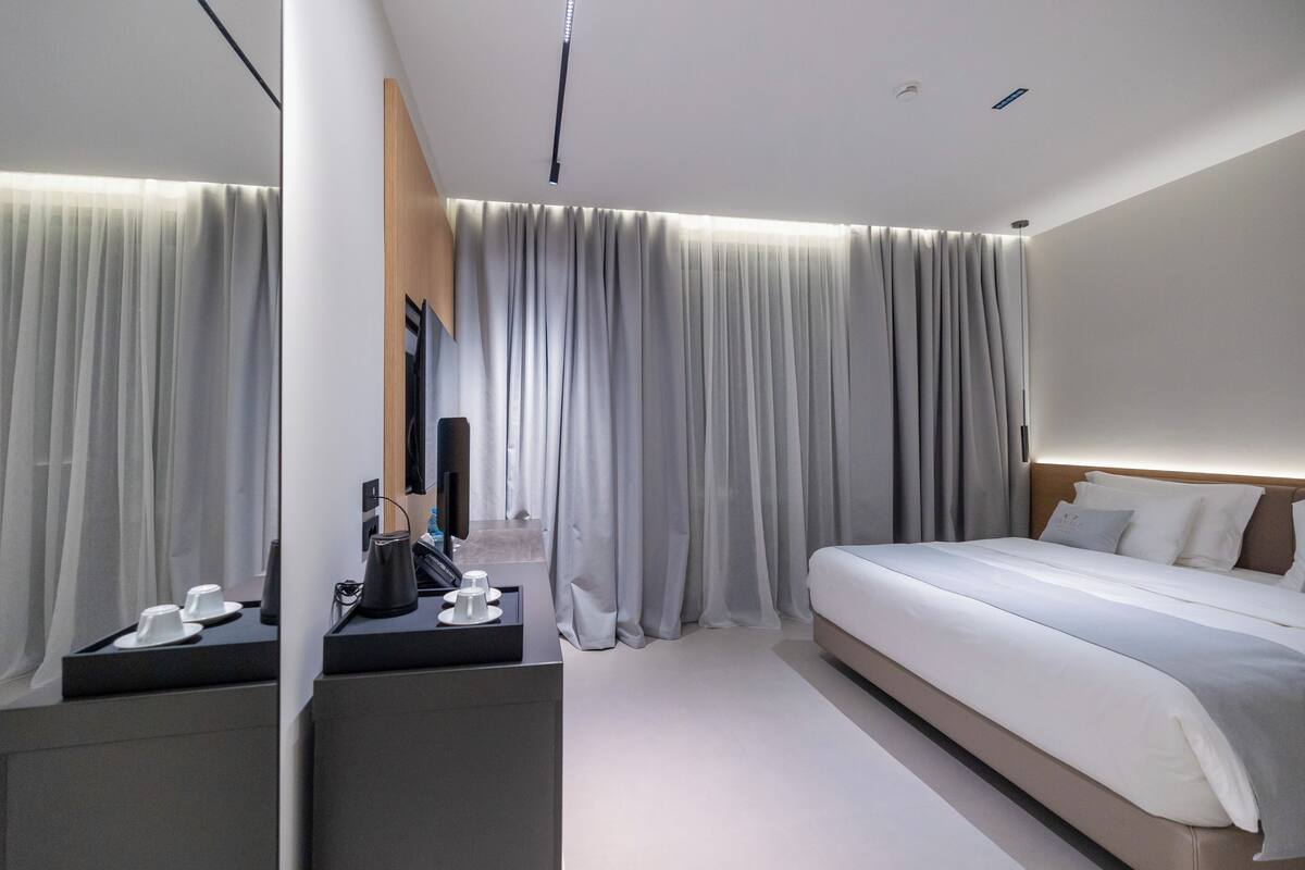 A modern hotel room with a bed, a desk, and a mirror.