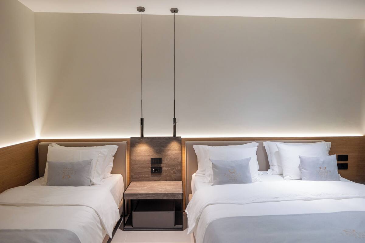 A hotel room with two beds, a wooden headboard, a nightstand, and a wall-mounted light fixture.