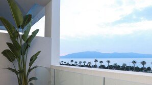 A balcony with a potted plant, a glass railing, and a view of a body of water and distant mountains. - Padma Hotel (Vlorë)