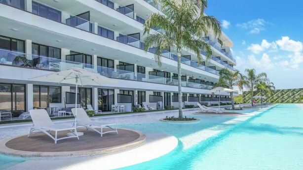 Un hôtel moderne doté d’une grande piscine, de chaises longues et de palmiers.