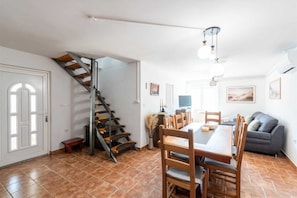 Ein Essbereich mit Holztisch und -stühlen, einer Treppe, einer Couch und einem Fernseher.