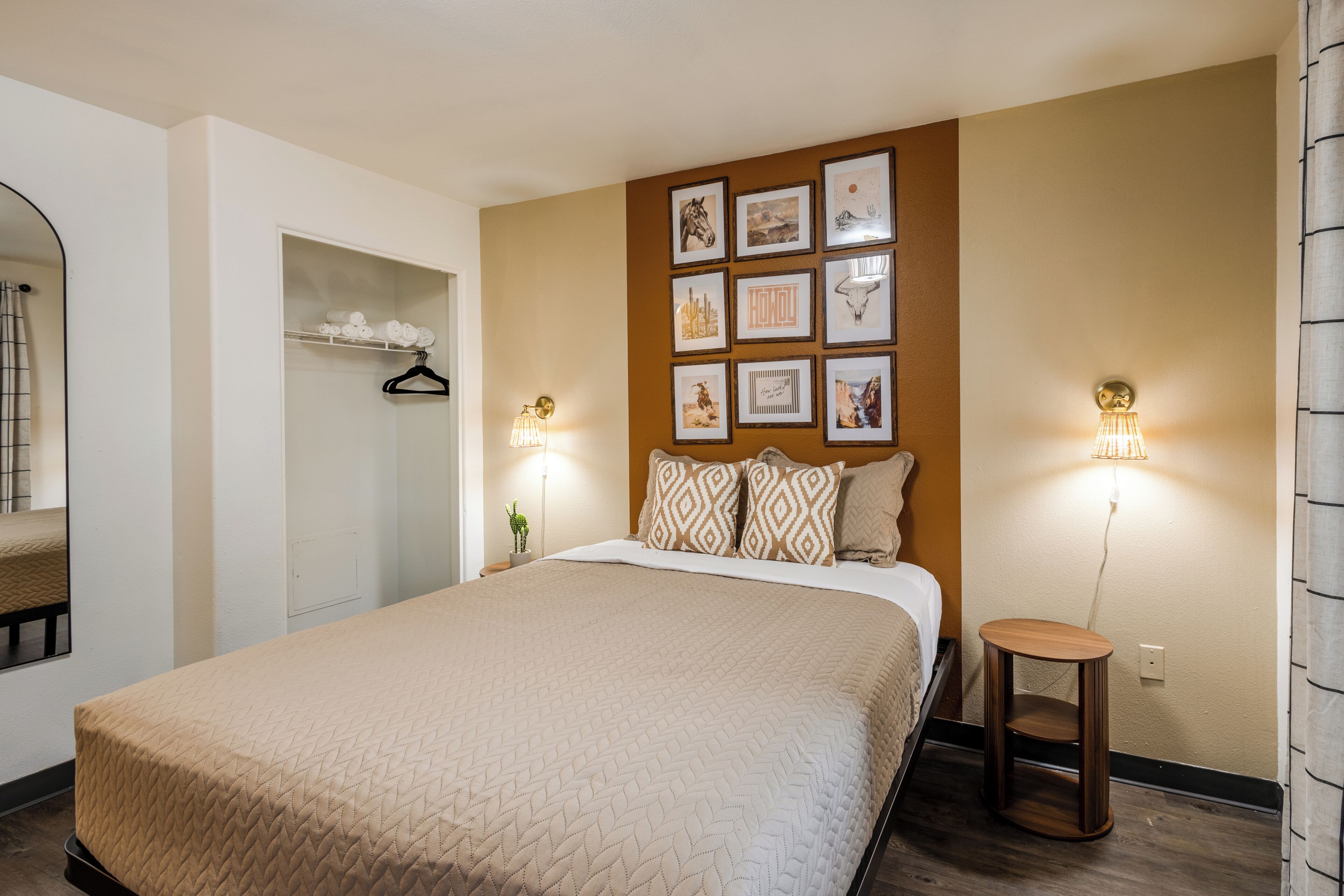 A bedroom with a large bed, a wardrobe, a small table, and wall-mounted lights.