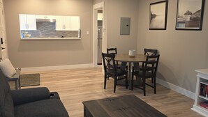 Ein Wohnzimmer mit einem dunkelbraunen Couchtisch, einem grauen Sofa und einem Essbereich mit Tisch und Stühlen.