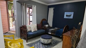 A room with a bed, a sofa, a wooden chair, a small table, and a rug. - The Pot Faerie Glen in Pretoria (Pretoria)