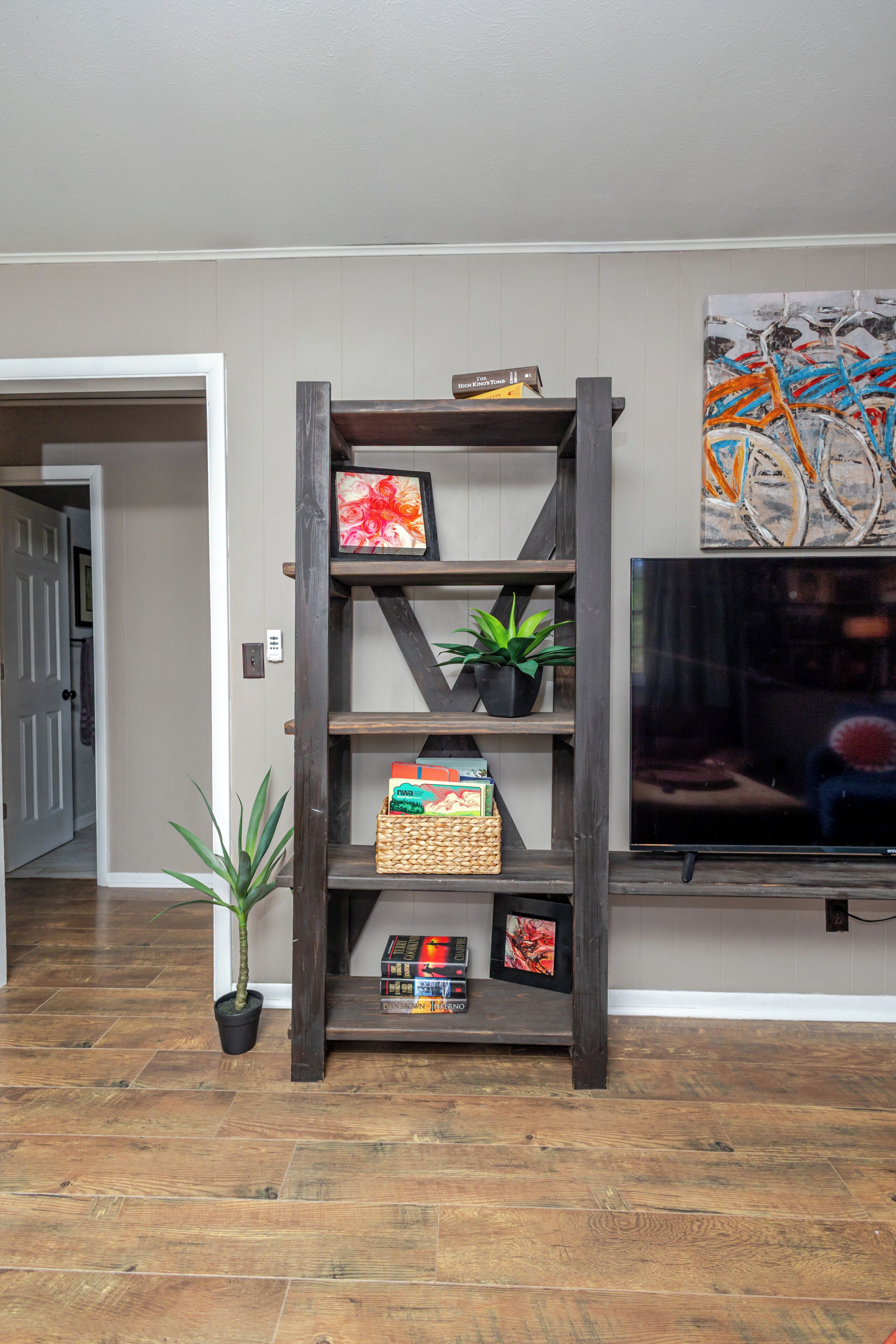 Un salon avec un meuble TV en bois, un téléviseur à écran plat, une plante en pot et une bibliothèque.