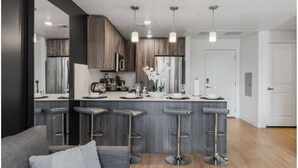 A modern kitchen with a central island, bar stools, stainless steel appliances, and pendant lighting.