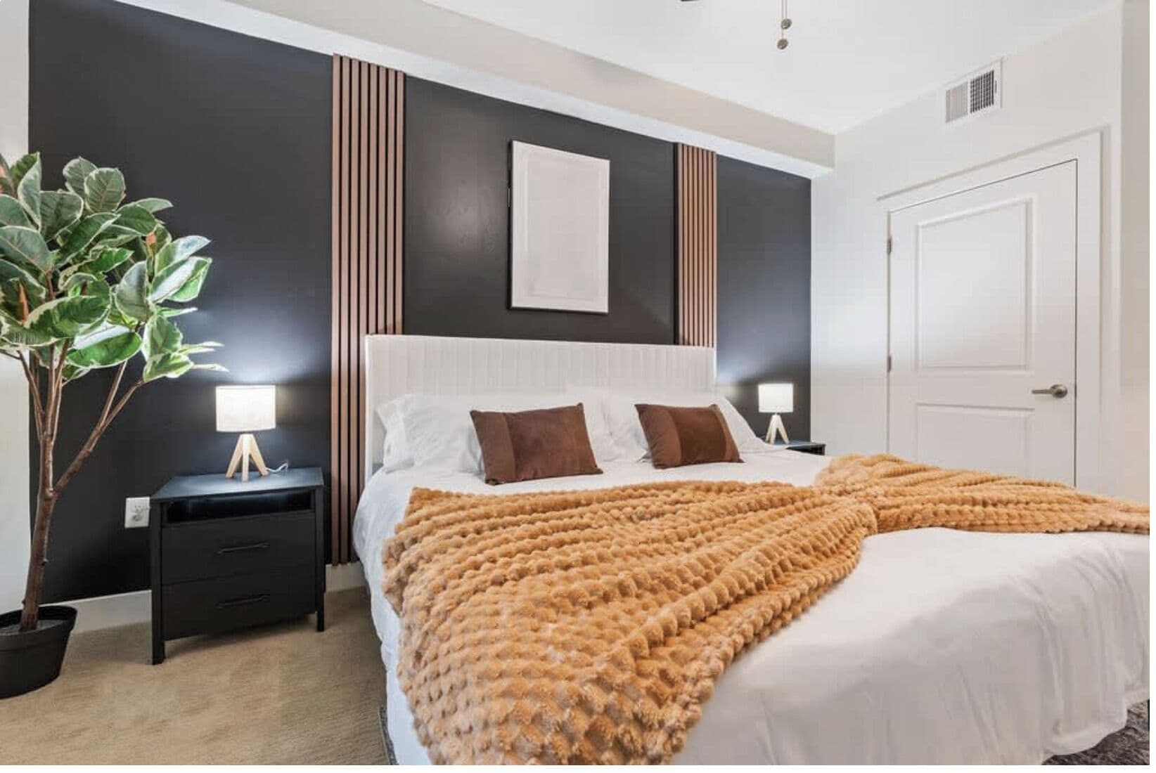 Une chambre à coucher moderne avec un grand lit, des tables de chevet, une plante en pot et un mur foncé orné de lignes verticales.