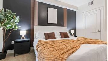 Une chambre à coucher moderne avec un grand lit, des tables de chevet, une plante en pot et un mur foncé orné de lignes verticales.