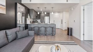 A modern kitchen with a central island, bar stools, and a dining area with a sofa and coffee table.