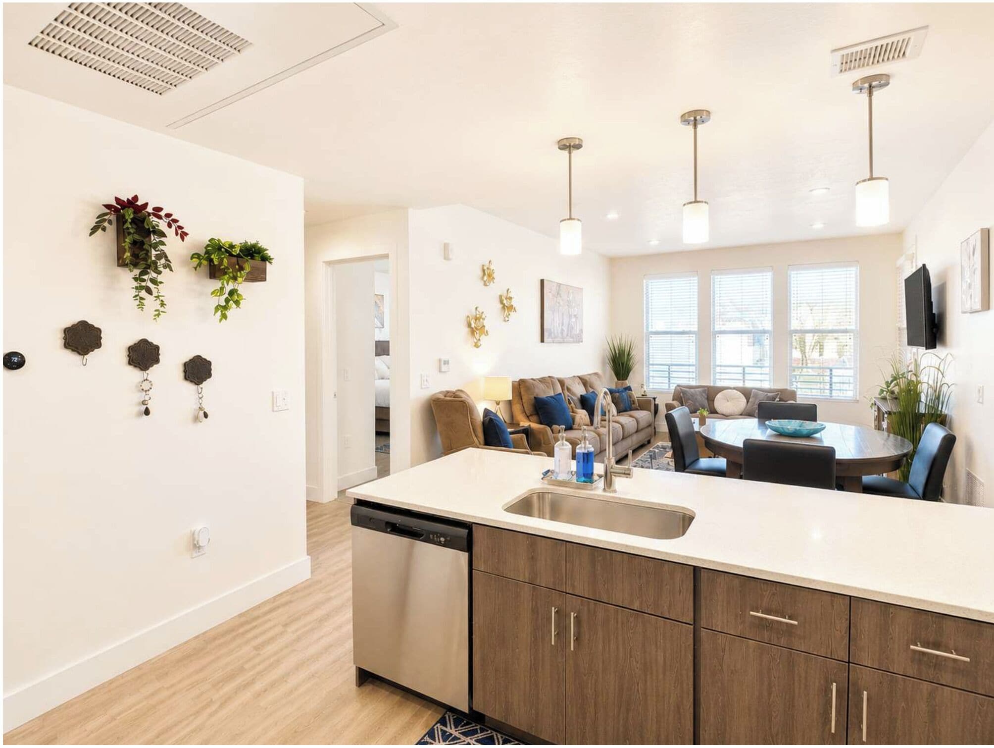 Una cocina moderna con lavavajillas, armarios de madera, una zona de comedor con mesa y sillas, y una sala de estar con sofá y televisor.