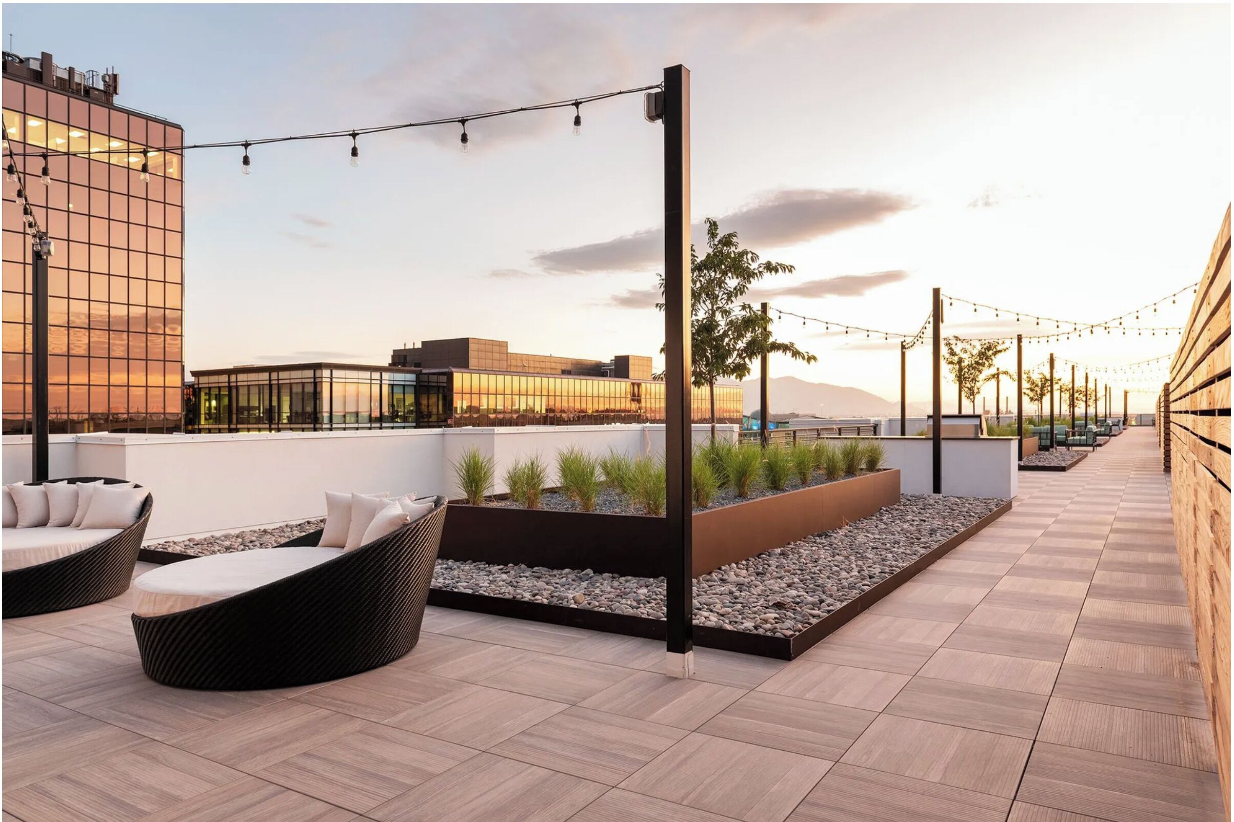 A rooftop terrace with outdoor seating, a view of buildings, and string lights.