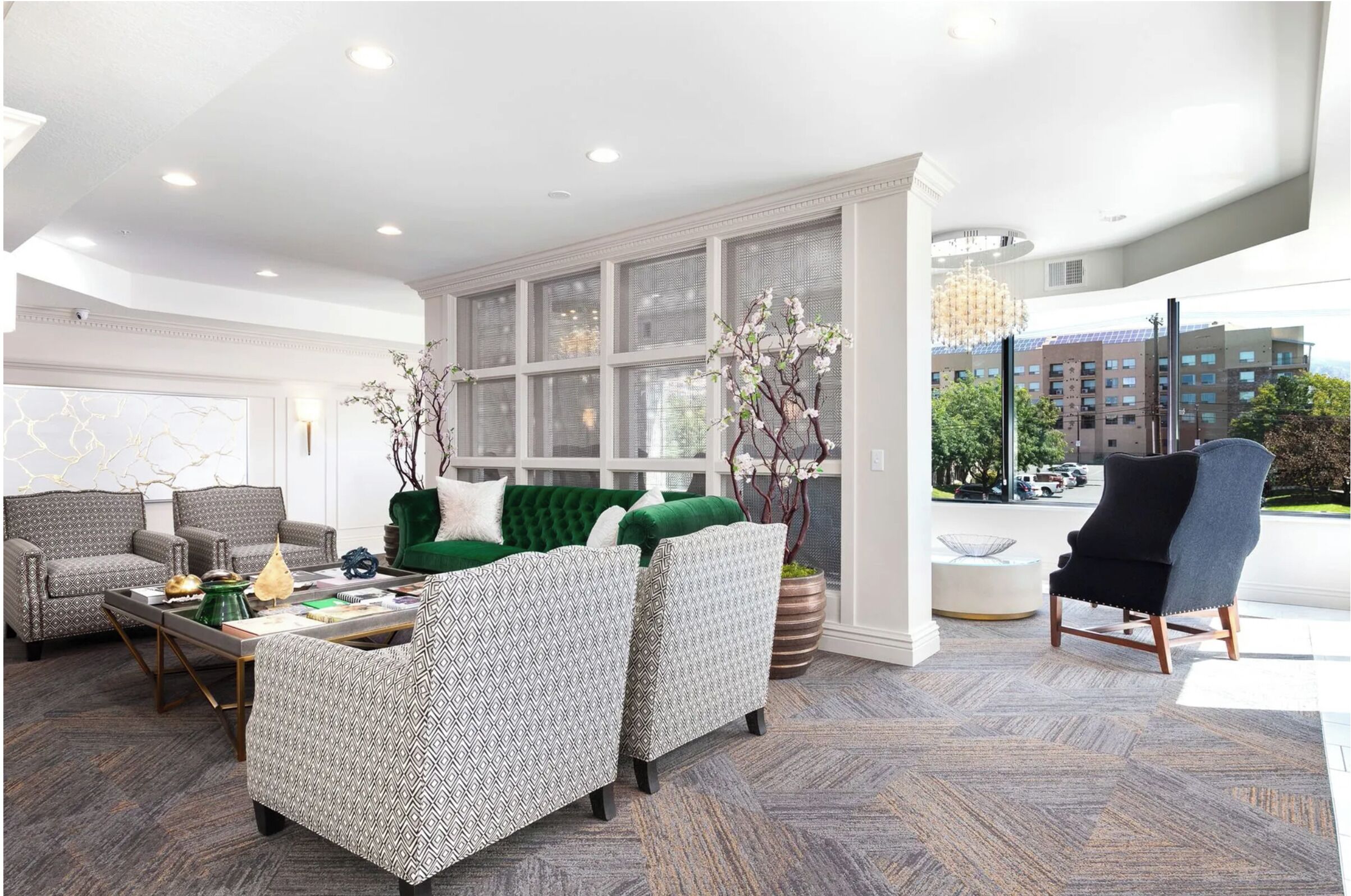 A modern living room with patterned furniture, a green sofa, and large windows offering a city view.