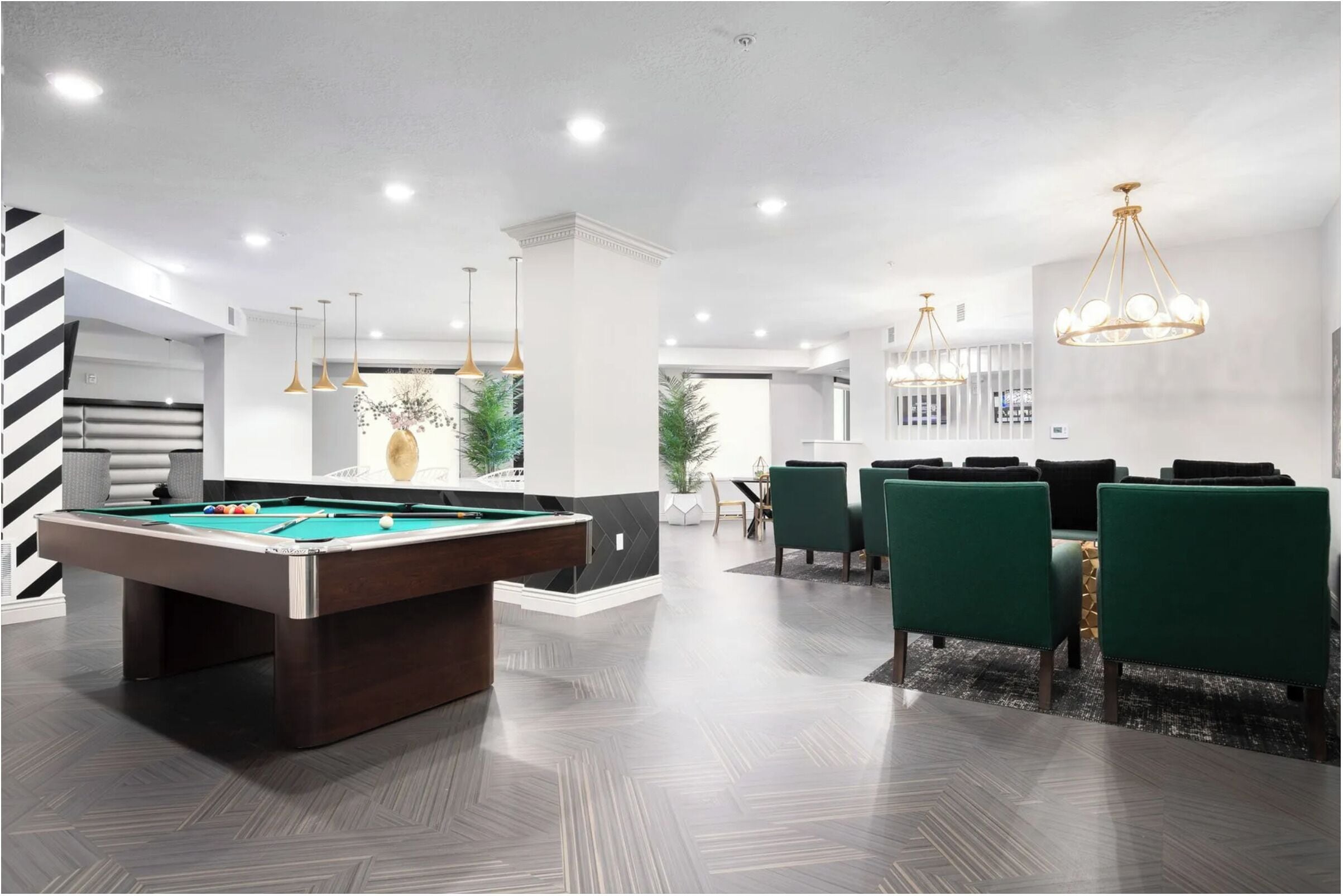 A modern indoor space with a pool table, green chairs, and a dining area with a chandelier.
