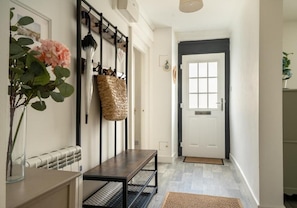A hallway with a bench, a coat rack with a woven bag, a door, and a framed picture on the wall.