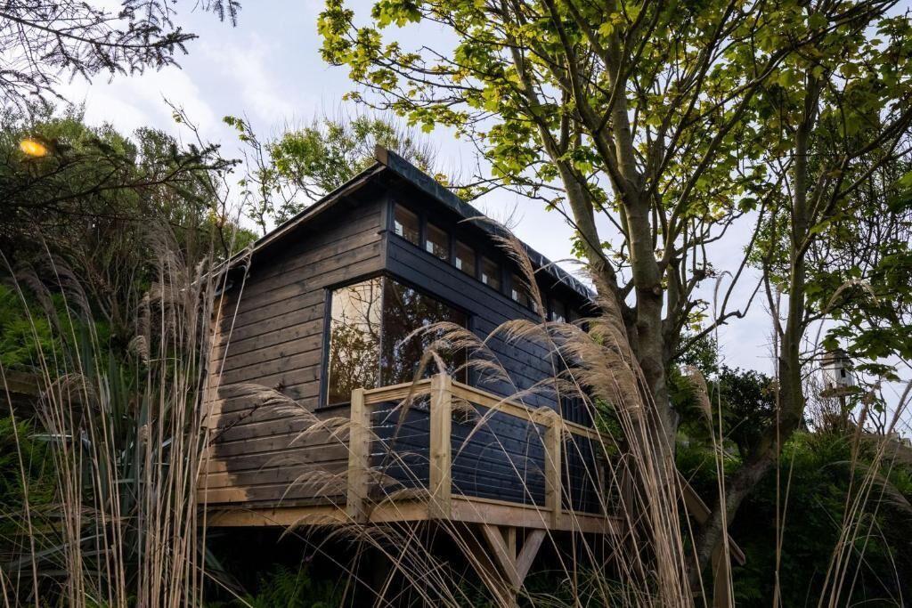 A wooden cabin with a balcony, surrounded by trees and tall grasses.