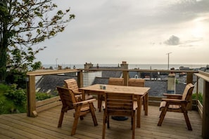 A wooden deck with a table and chairs, overlooking a cityscape and the sea.