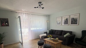 Uma sala de estar com sofá, pufes, mesa de centro e luminária.