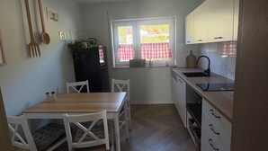 Uma cozinha compacta com mesa e cadeiras, janela com cortinas e forno embutido.